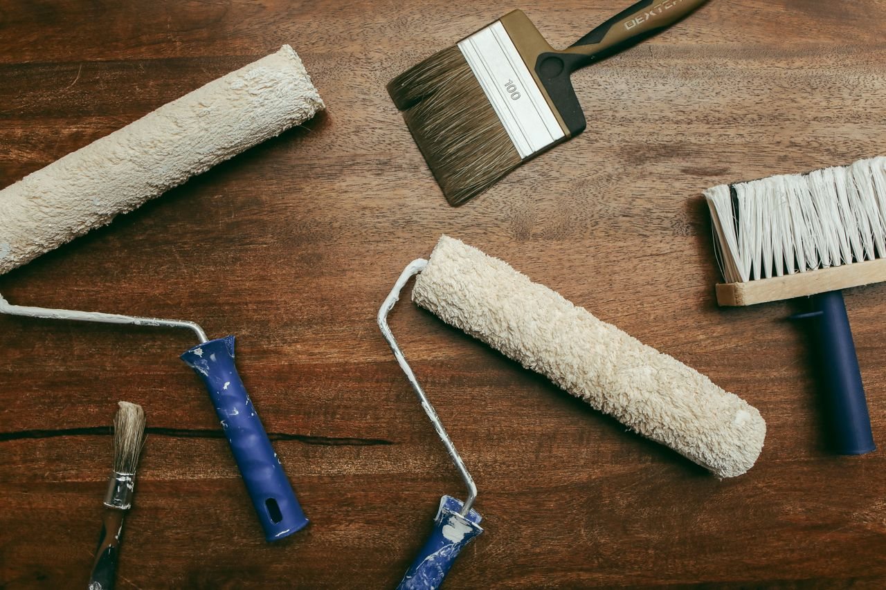 Free Top view of various painting tools including rollers and brushes laid out on a wooden surface. Stock Photo