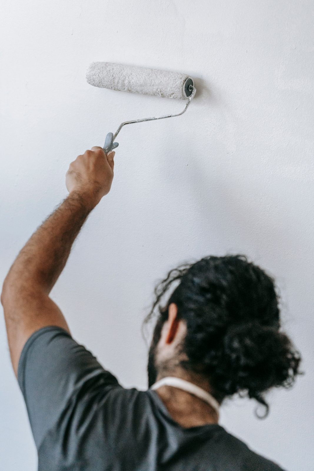 A man painting a wall white with a roller, focusing on home renovation